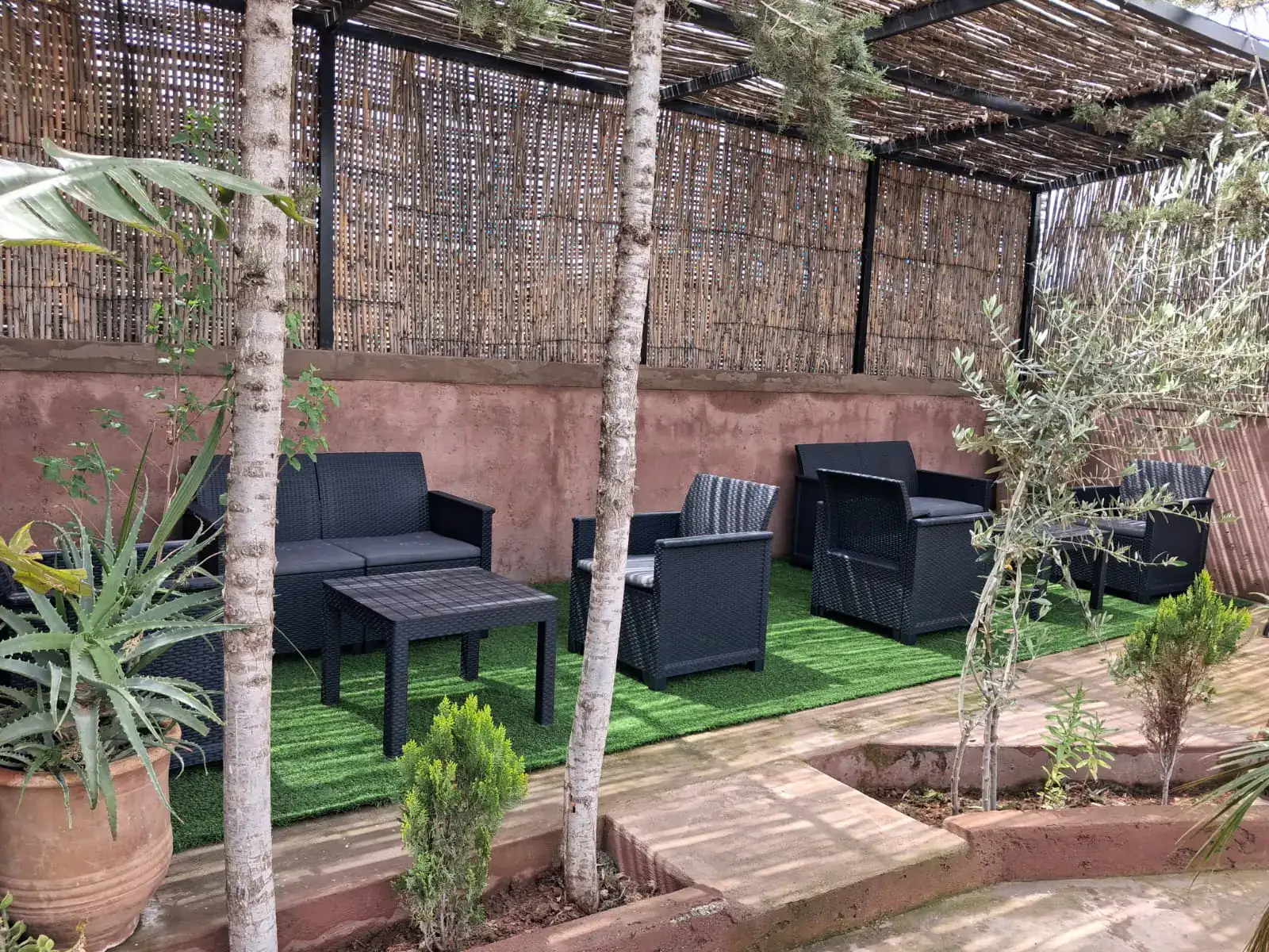 Shaded outdoor lounge at Chambre d’hôtes Aya with wicker armchairs beneath a reed pergola